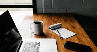 MacBook Pro, white ceramic mug,and black smartphone on table